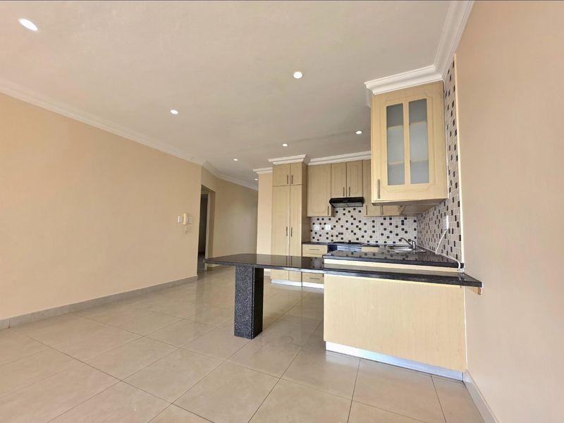 Open-plan kitchen and living area featuring light wood cabinetry, granite countertops, a breakfast bar, and neutral tiled flooring throughout.