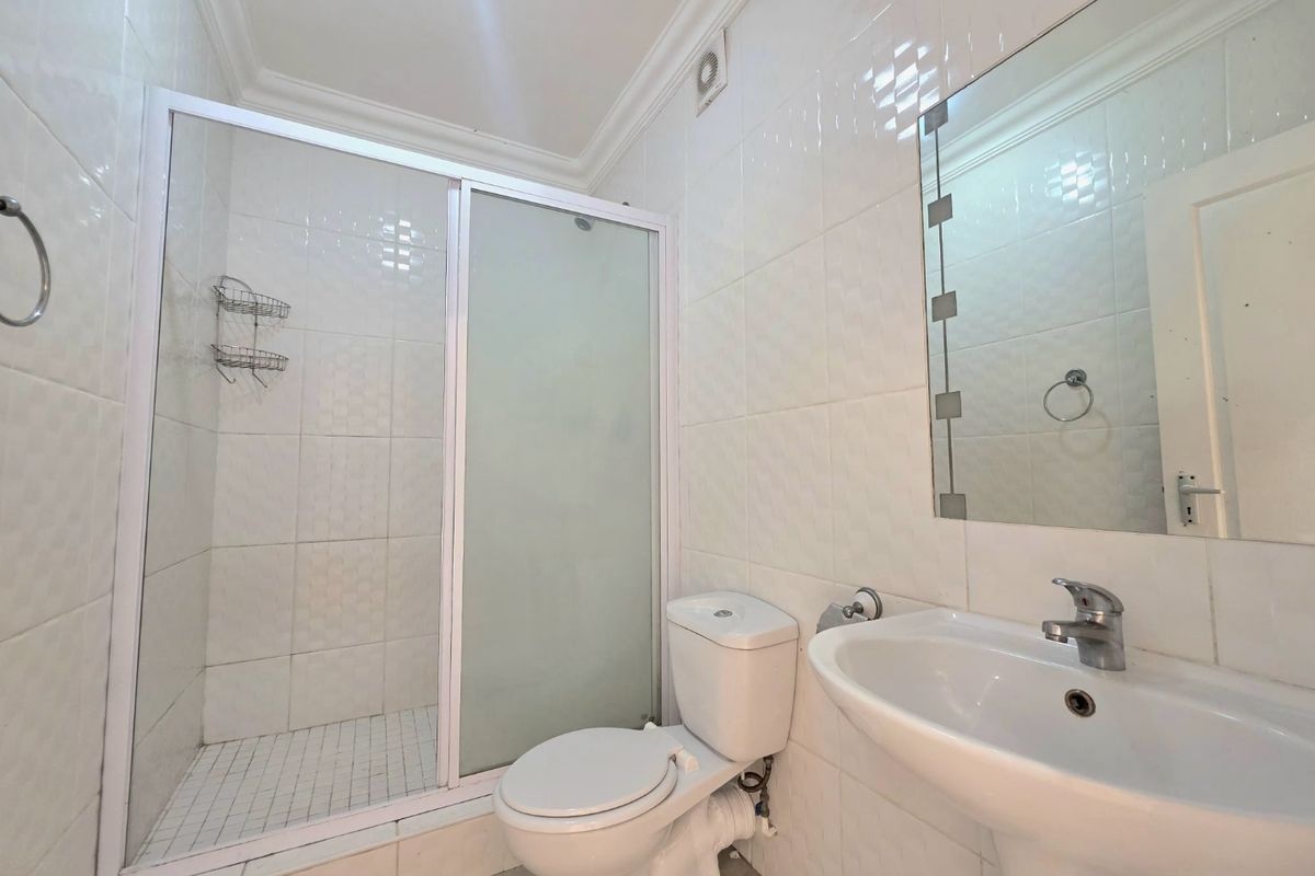 A functional bathroom featuring a shower enclosure, pedestal basin, toilet, and wall-mounted mirror with fully tiled walls.