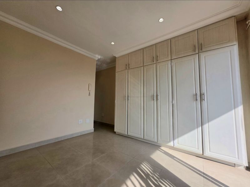 A bright, empty bedroom featuring neutral tiled flooring, recessed downlighting, and extensive built-in cabinetry with classic panel detailing.