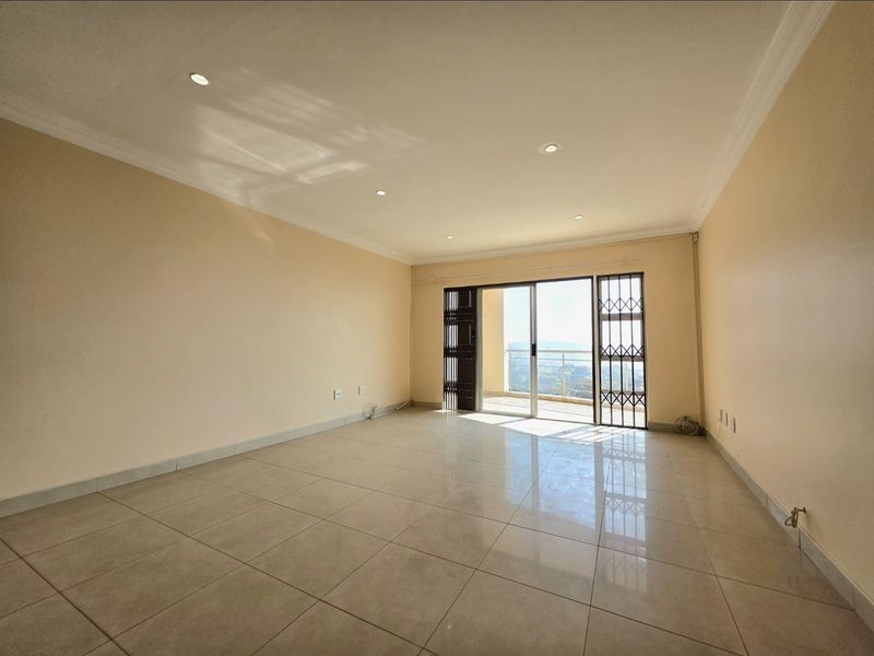 Spacious, light-filled living area featuring neutral tiled floors, recessed lighting, and direct access to a balcony through a sliding glass door.
