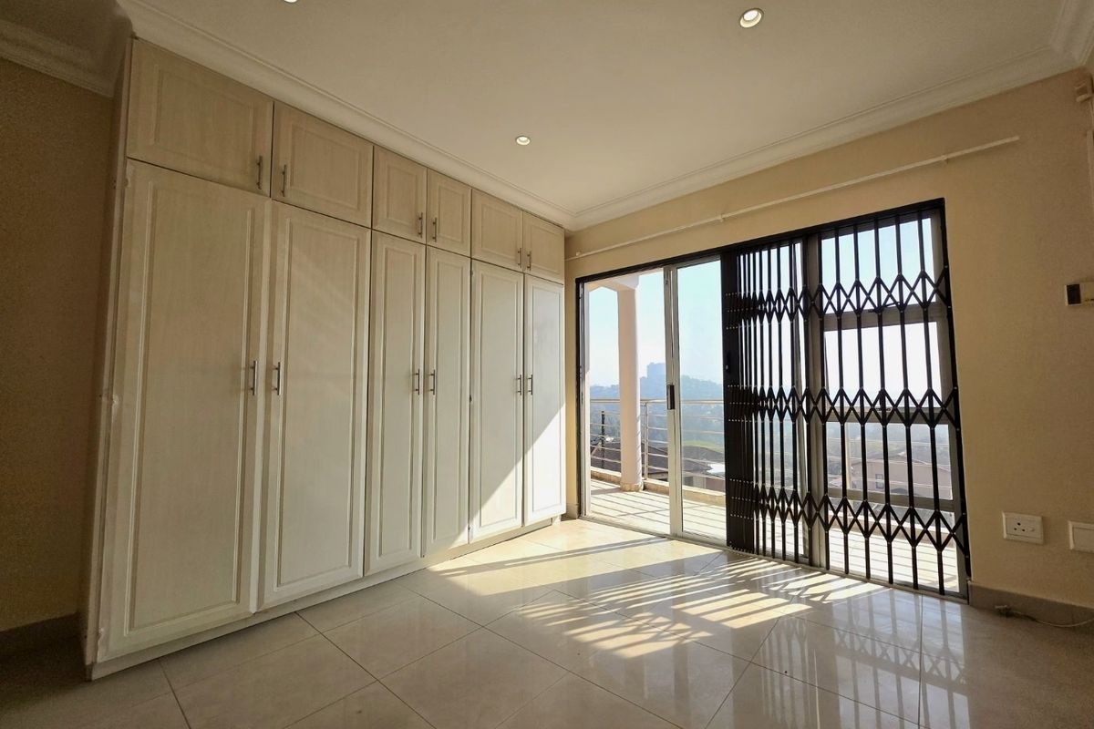 A bright, empty bedroom featuring extensive built-in cabinetry, tiled flooring, and a sliding glass door leading to a balcony with security gate.