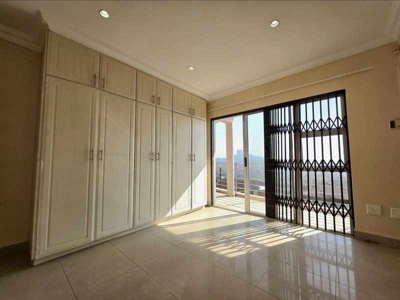 A bright, empty bedroom featuring extensive built-in cabinetry, tiled flooring, and a sliding glass door leading to a balcony with security gate.