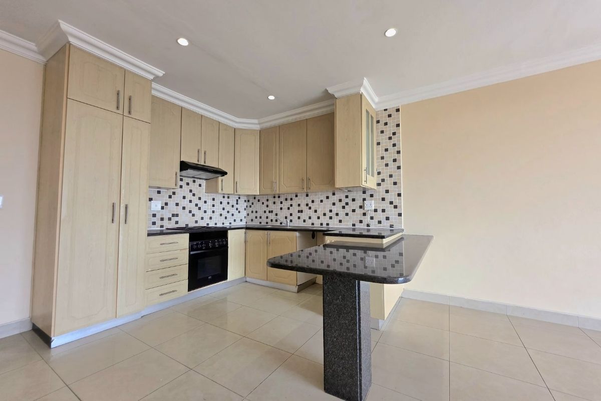 A clean, empty kitchen featuring light wood cabinetry, granite countertops with a breakfast bar, and a tiled backsplash.