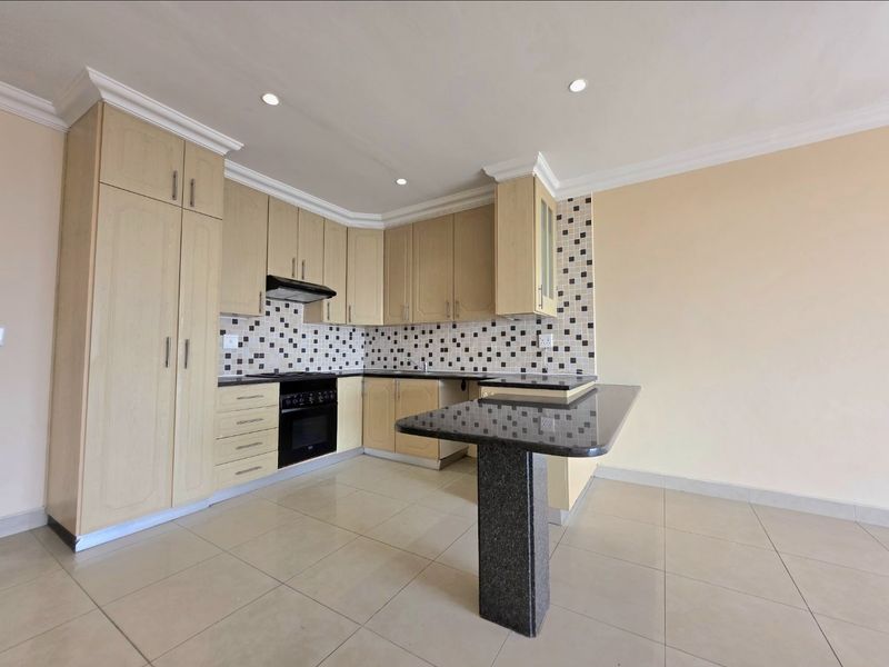 A clean, empty kitchen featuring light wood cabinetry, granite countertops with a breakfast bar, and a tiled backsplash.