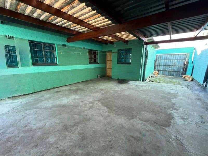 A covered outdoor patio area featuring concrete flooring, timber roof beams, and security bars on the windows.