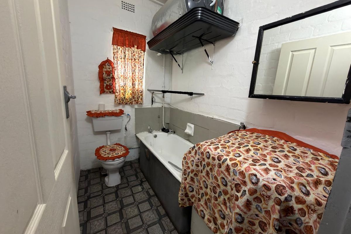 A compact bathroom featuring a bathtub, toilet, and wall-mounted electric water heater, requiring modernization of finishes and fixtures.