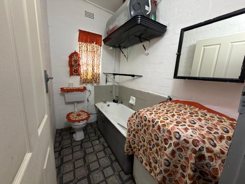 A compact bathroom featuring a bathtub, toilet, and wall-mounted electric water heater, requiring modernization of finishes and fixtures.