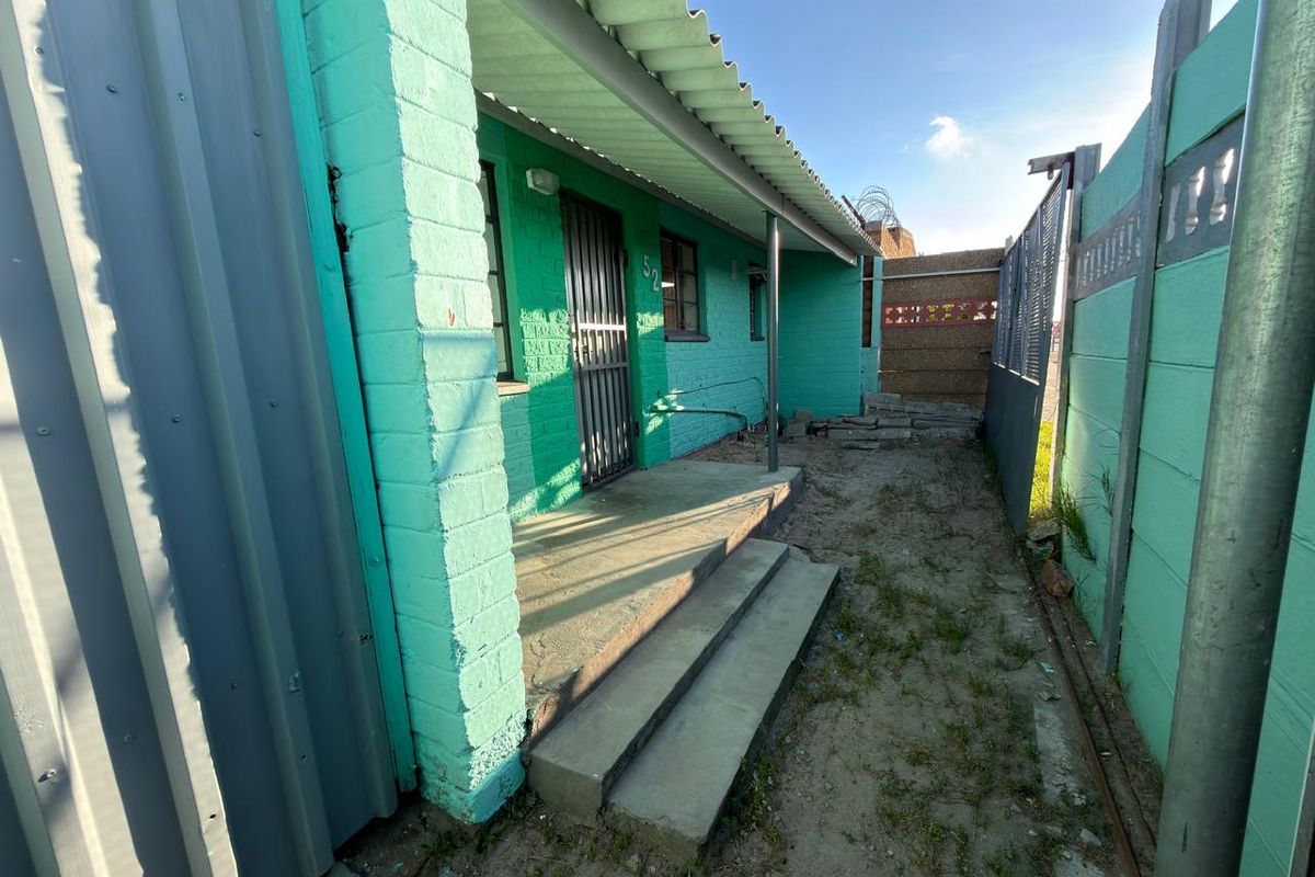 A side view of the property showing a concrete entrance path, security gate, and perimeter walling with a corrugated metal roof overhang.