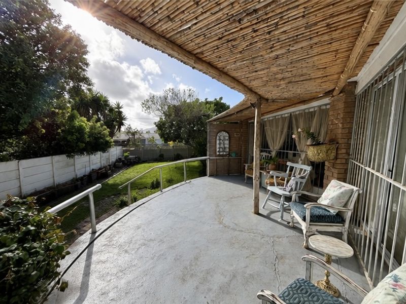 Covered patio area featuring a bamboo roof structure, concrete flooring, and metal railings, overlooking a private garden space.