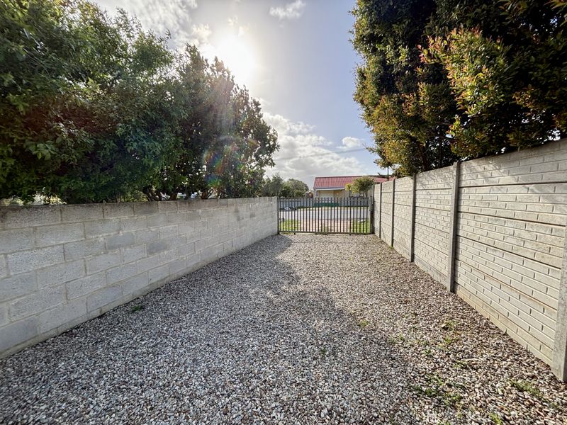 A private rear outdoor area featuring gravel surfacing, enclosed by concrete block boundary walls and secured with a metal gate.