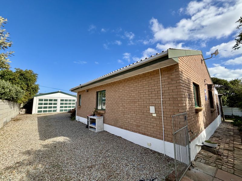 Rear view of the brick house featuring a gravel driveway, detached garage, and paved walkway area.