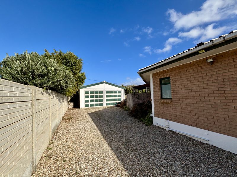 Rear exterior view showing a brick house facade, gravel driveway, and a detached garage with a precast concrete boundary wall.