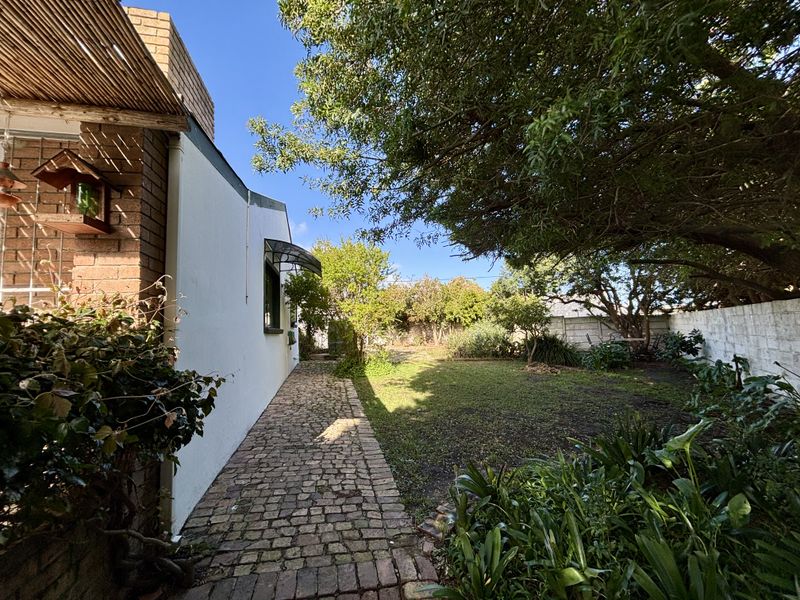 A private rear garden featuring a brick-paved pathway, established trees, and a secure boundary wall.