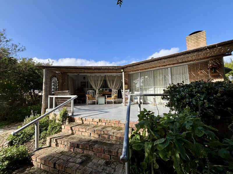 A covered outdoor patio area featuring brick stairs, metal handrails, and sliding glass doors leading into the home, with a rustic thatched roof finish.