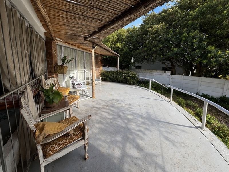 A covered patio area featuring a thatched roof, concrete flooring, and metal railings, providing direct access to the home through sliding glass doors.