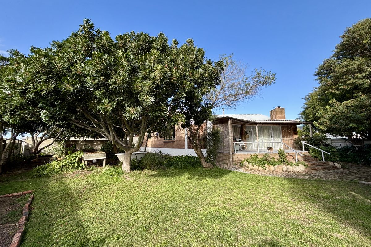 Rear view of the house featuring a covered patio, brick chimney, and a spacious garden with mature trees and brick paving.