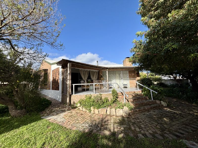 Rear view of the house featuring a covered veranda, brick patio area, and established garden surroundings.
