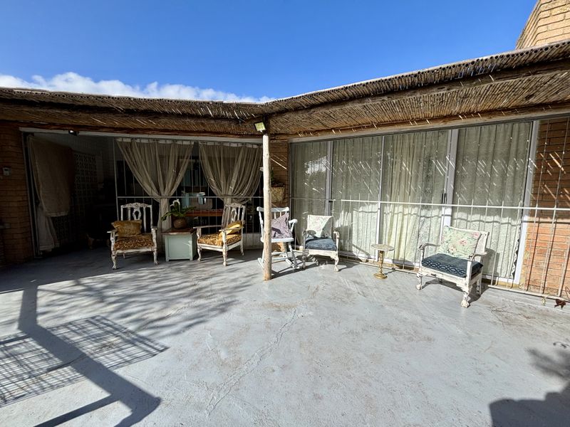 A covered outdoor patio area featuring a thatched roof, concrete flooring, and sliding glass doors with security gates.