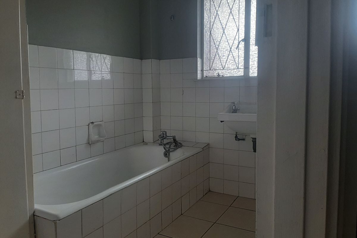 A dated bathroom featuring a built-in bathtub, wall-mounted basin, and tiled finishes, offering a blank canvas for a modern renovation.