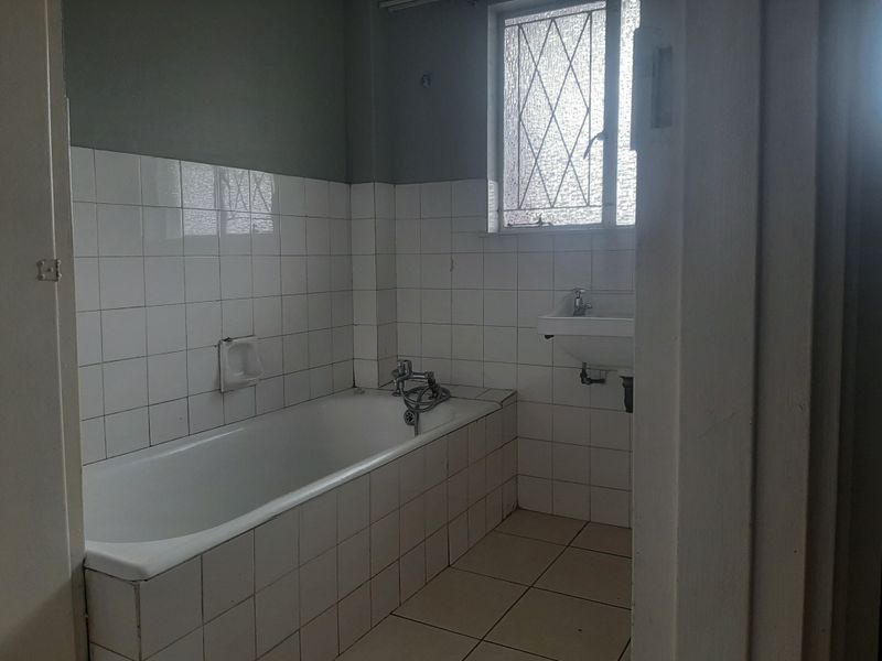 A dated bathroom featuring a built-in bathtub, wall-mounted basin, and tiled finishes, offering a blank canvas for a modern renovation.