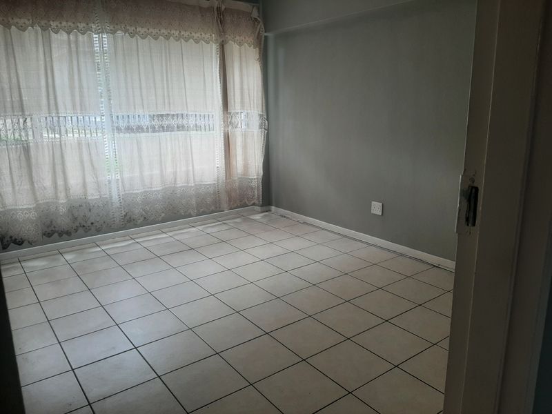 An empty bedroom featuring neutral grey walls, tiled flooring, and a large window with security bars, offering a blank canvas for personalization.