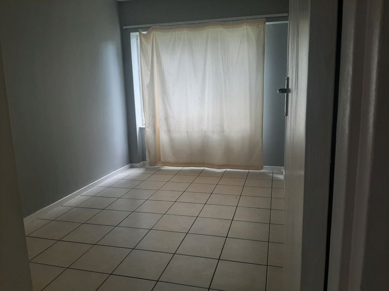An empty bedroom featuring neutral grey walls and tiled flooring, providing a blank canvas for personalization.