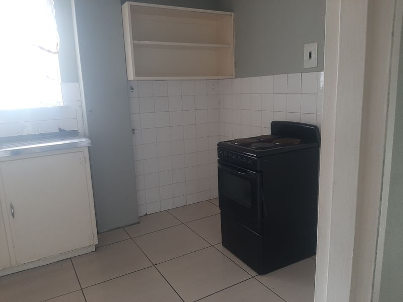 A functional kitchen space featuring tiled flooring, a tiled splashback, a freestanding stove, and built-in shelving, ready for modernization.