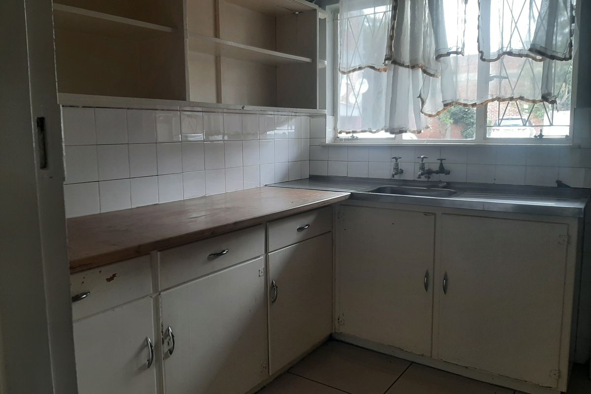 A dated, empty kitchen featuring original built-in cabinetry, a stainless steel sink, and tiled finishes, offering significant potential for renovation and modernization.