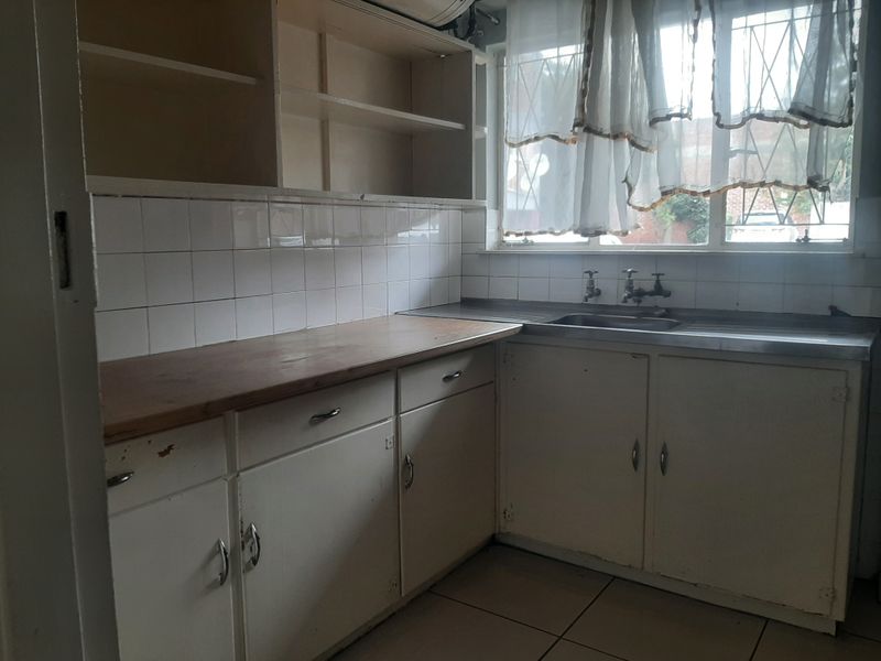 A dated, empty kitchen featuring original built-in cabinetry, a stainless steel sink, and tiled finishes, offering significant potential for renovation and modernization.