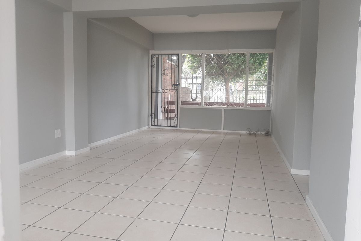 A spacious, empty living area featuring neutral grey walls, tiled flooring, and a secure entrance with security gate and window bars.