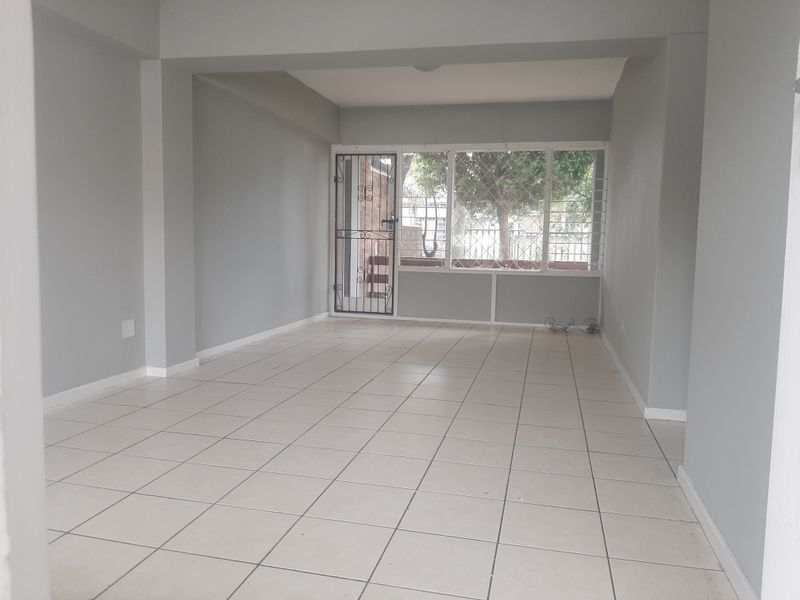 A spacious, empty living area featuring neutral grey walls, tiled flooring, and a secure entrance with security gate and window bars.