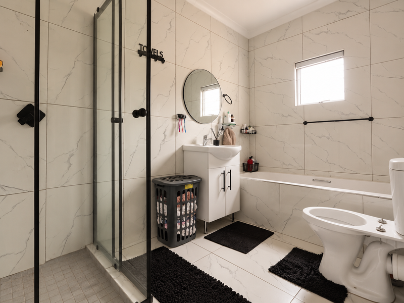 Modern bathroom featuring a walk-in shower with glass enclosure, a built-in bathtub, vanity with basin, and toilet, finished with elegant marble-look wall tiles.