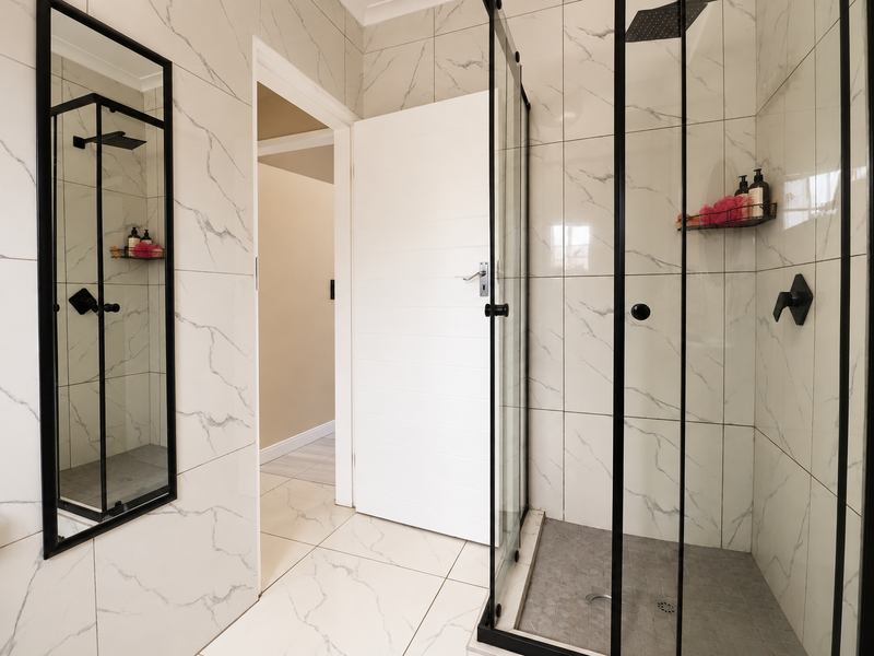 Modern bathroom featuring a walk-in shower with a black-framed glass enclosure, rain shower head, and elegant marble-look wall tiling.