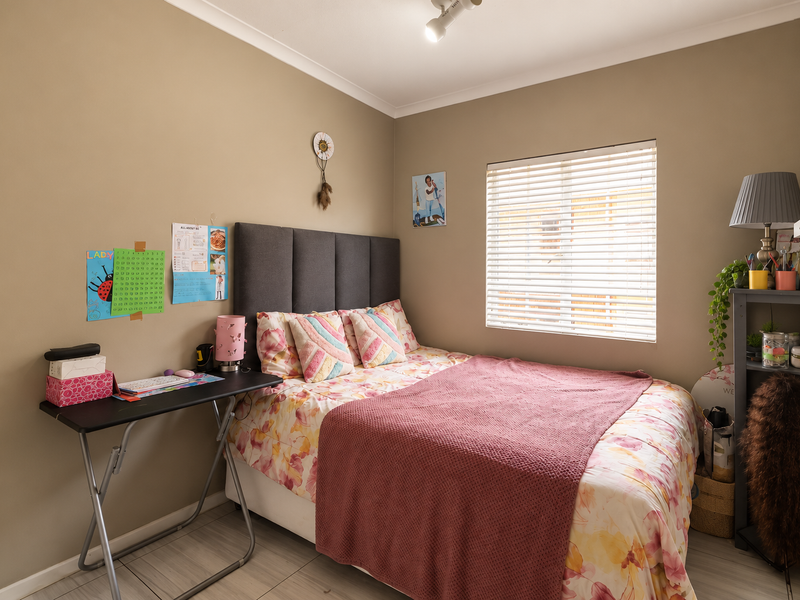 A well-maintained bedroom featuring neutral wall tones, tiled flooring, and a window fitted with venetian blinds.