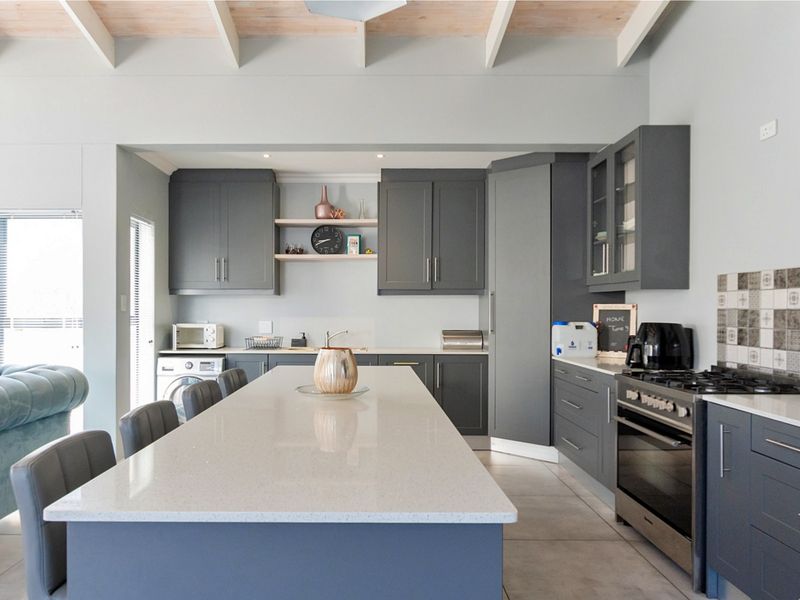 Modern kitchen featuring dark grey cabinetry, a large central quartz island, gas stove, and exposed ceiling beams, creating a functional and stylish cooking space.