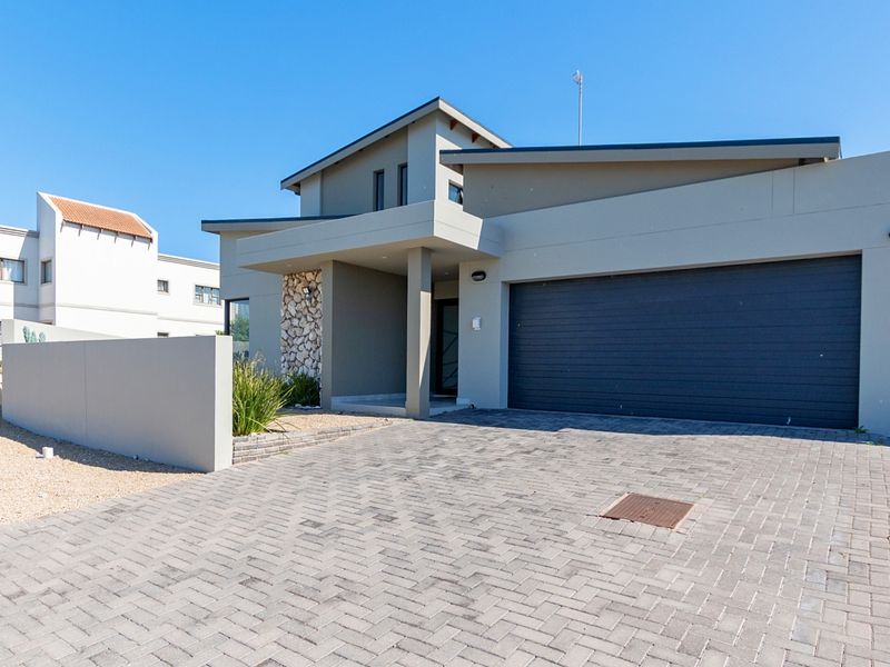 Modern front elevation featuring a paved driveway, double garage, and a distinctive stone-clad entrance pillar.
