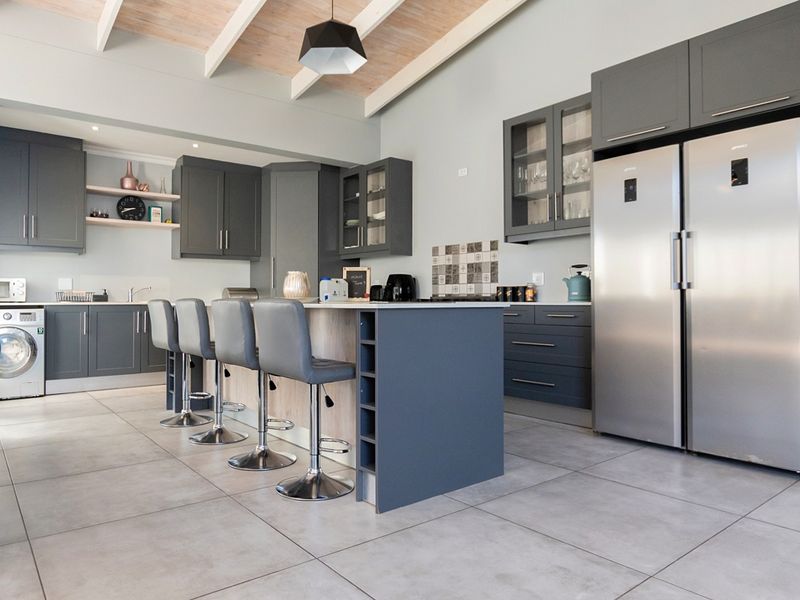 Modern kitchen featuring dark grey cabinetry, a central island with breakfast bar seating, tiled floors, and an exposed beam ceiling.