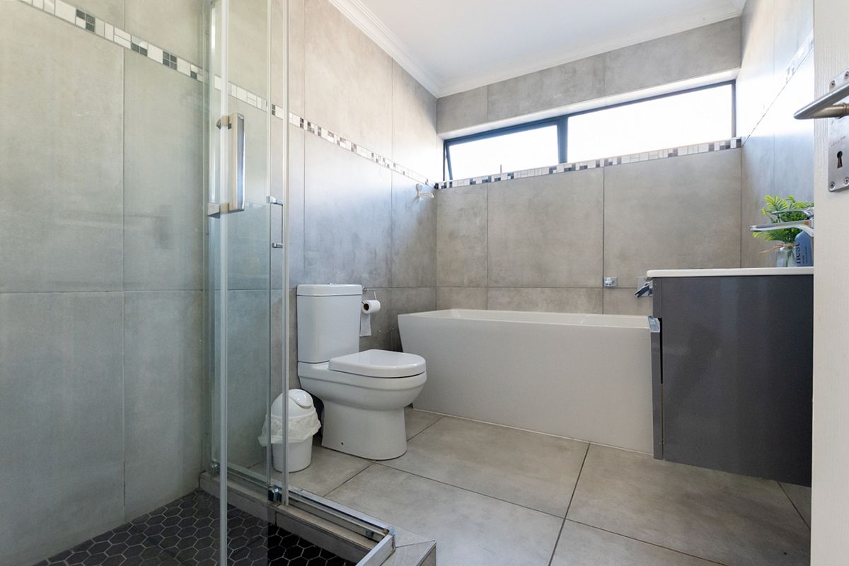 Modern bathroom featuring a glass-enclosed shower, a built-in bathtub, a vanity cabinet, and neutral grey wall and floor tiling.