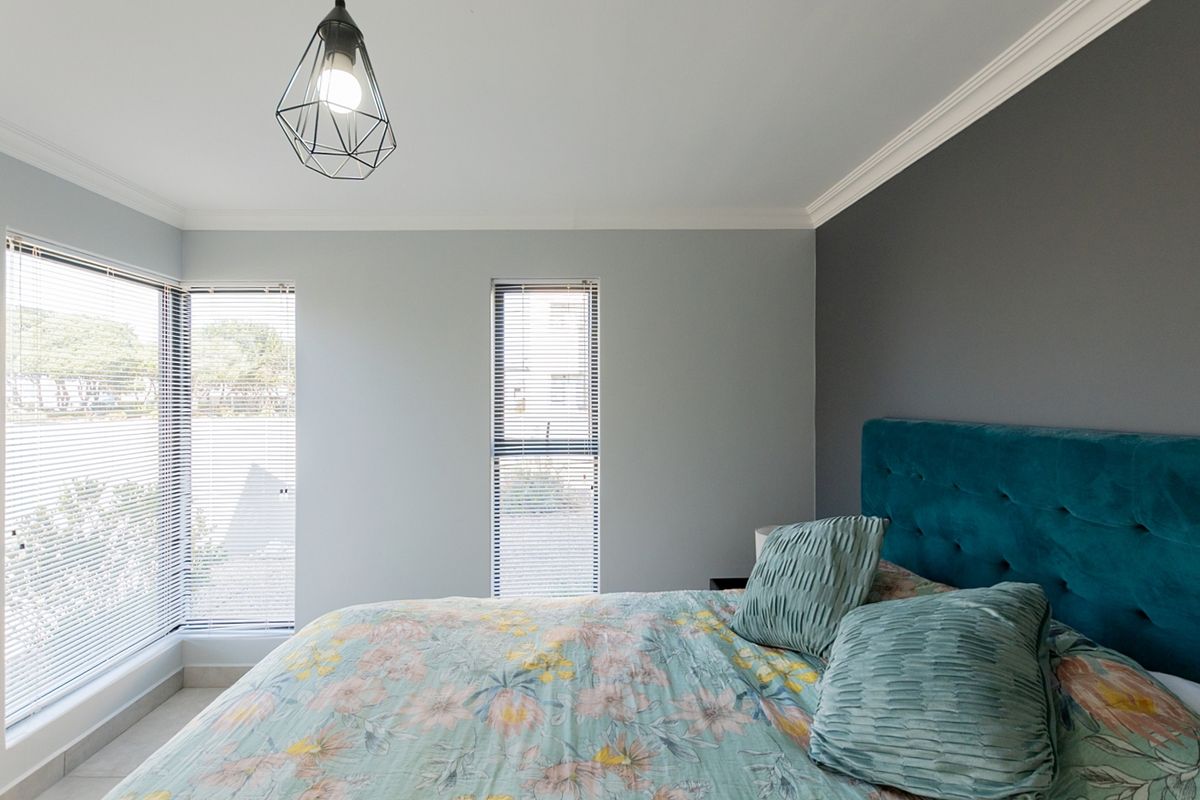A well-maintained bedroom featuring modern grey and dark accent walls, large windows with fitted venetian blinds, and decorative cornice detailing.