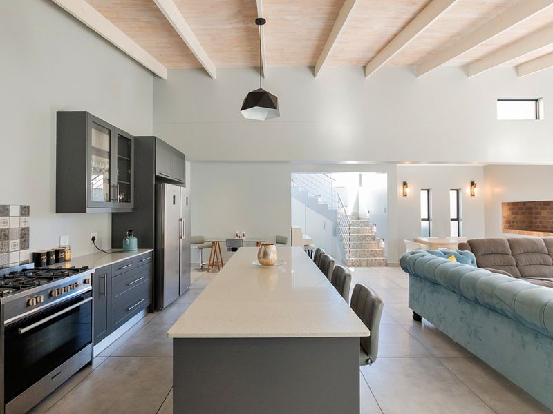 Spacious open-plan living area featuring a modern kitchen with a central island, gas stove, and high exposed beam ceilings leading to a staircase.