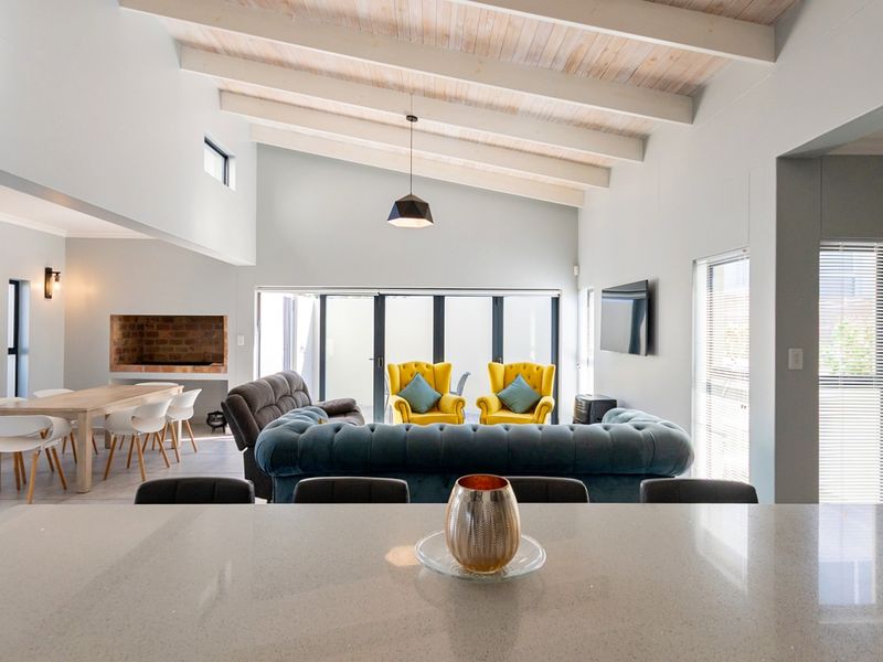 Spacious open-plan living and dining area featuring high vaulted ceilings with exposed timber beams, a built-in brick fireplace, and seamless access to the outdoors.