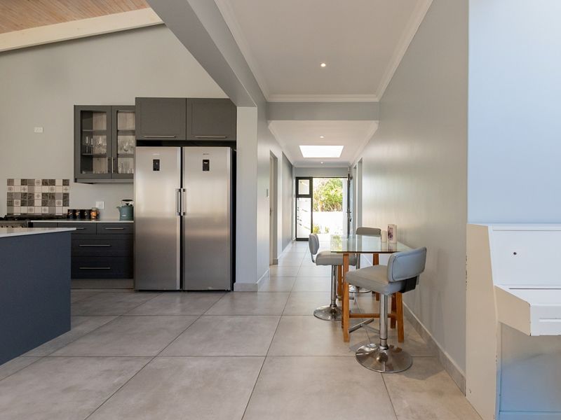 Modern open-plan kitchen and dining area featuring sleek cabinetry, large format floor tiles, a vaulted ceiling, and a bright skylight.