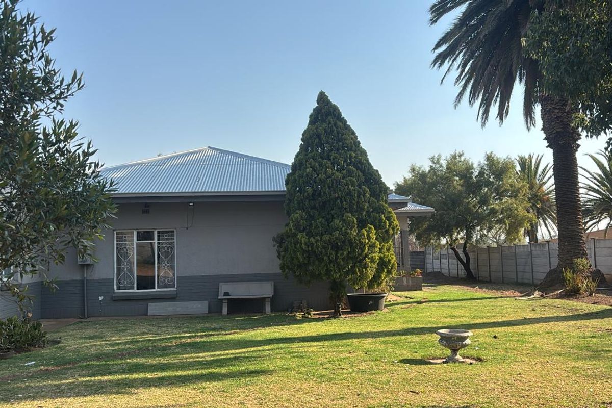 A view of the rear exterior of the house featuring a metal roof, security-barred windows, and a spacious garden with a concrete boundary wall.