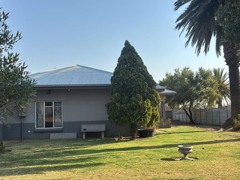 A view of the rear exterior of the house featuring a metal roof, security-barred windows, and a spacious garden with a concrete boundary wall.