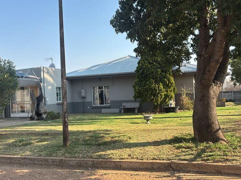 Front view of a single-story house featuring a metal roof, security bars on windows, and a spacious front garden area.