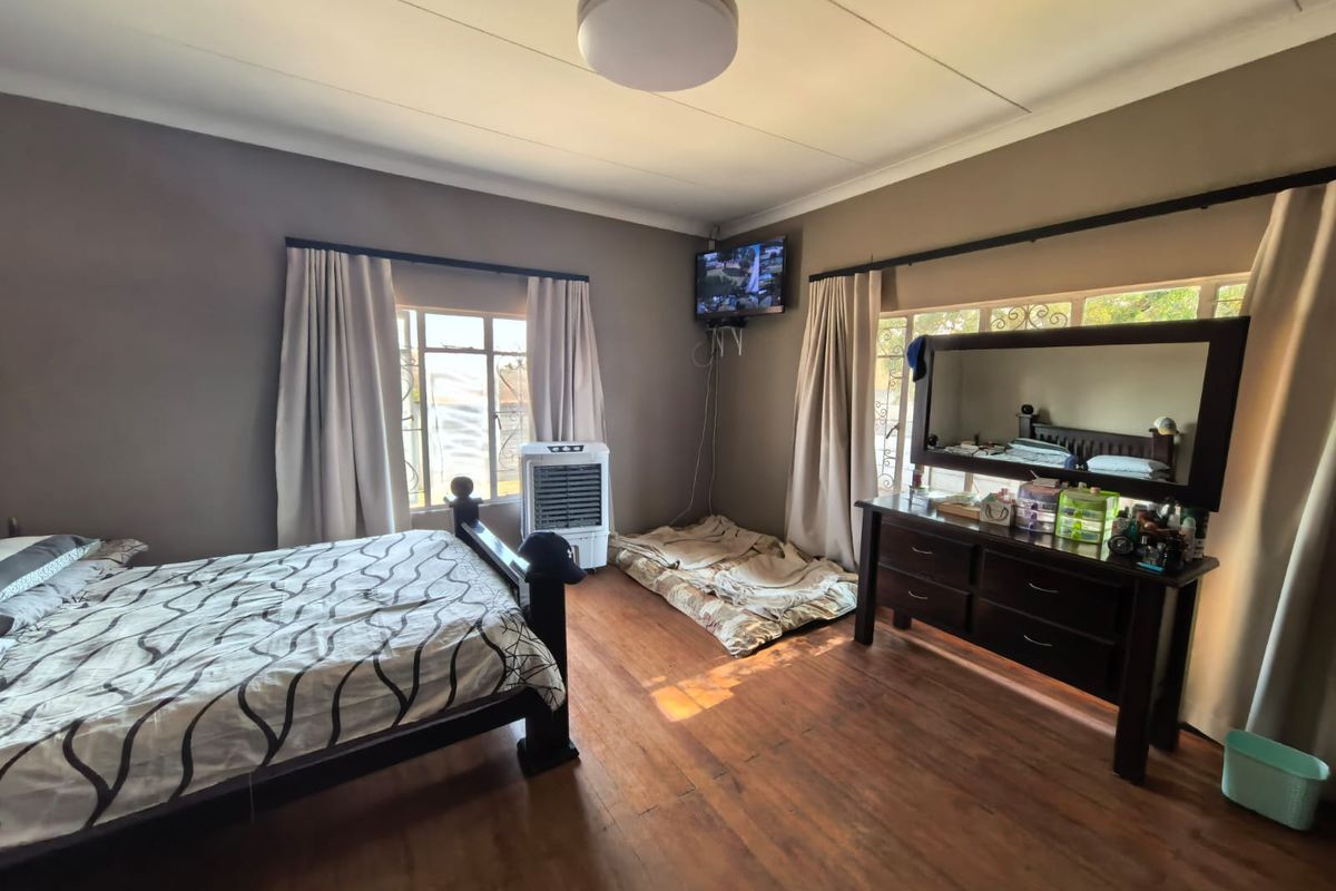 Spacious bedroom featuring hardwood flooring, large windows with security bars, and neutral wall tones, offering a comfortable and functional living space.