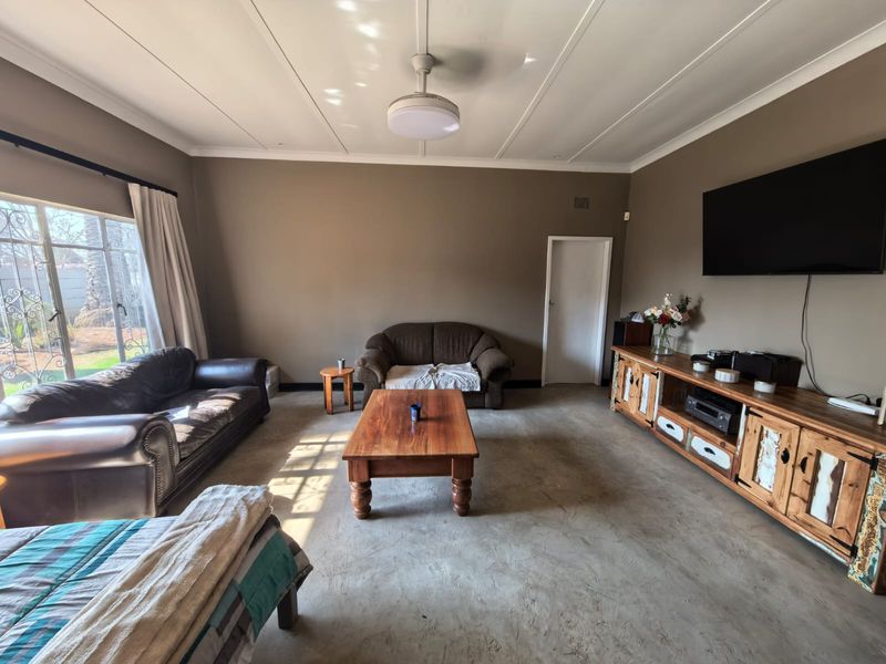 Spacious living room featuring concrete flooring, a ceiling fan, and large sliding glass doors providing natural light and garden access.