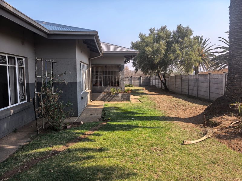 Rear view of the property featuring a lawn, concrete pathway, and precast concrete boundary wall with security bars on the windows.