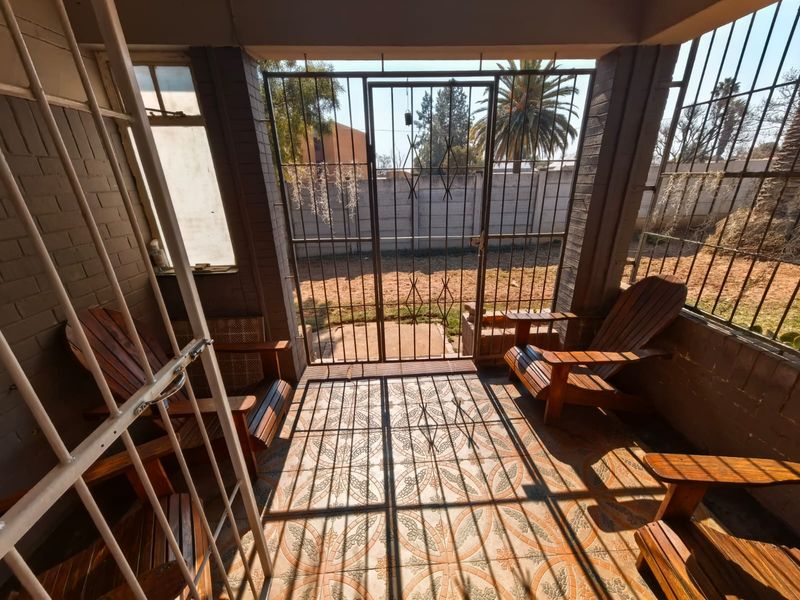 A covered patio area featuring tiled flooring, brick pillars, and extensive security bars and gates overlooking the rear garden.