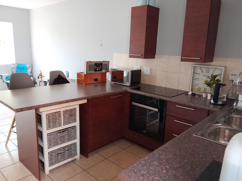 Open plan kitchen featuring dark wood cabinetry, laminate countertops, integrated oven and hob, and tiled flooring, seamlessly connecting to the living area.